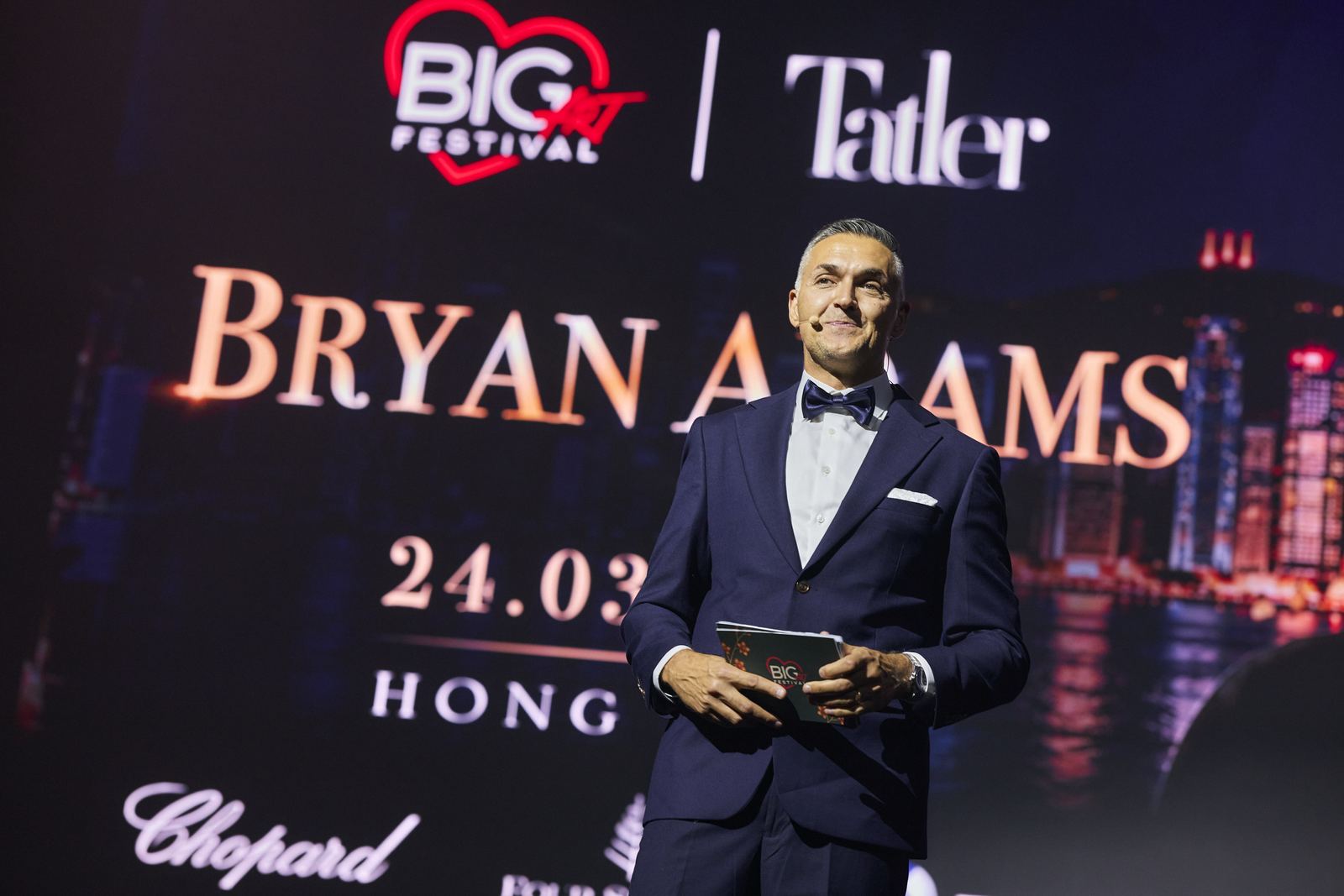 Ведущий объявляет Big Art Festival Hong Kong с Bryan Adams на экранах.