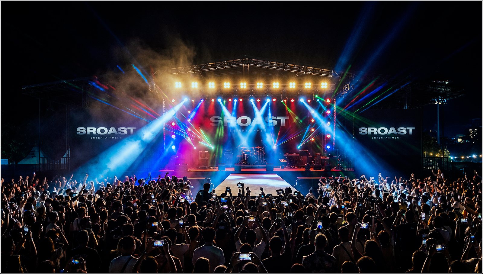 Show night from the floor — full stage with the rig lit, beams over a packed crowd.