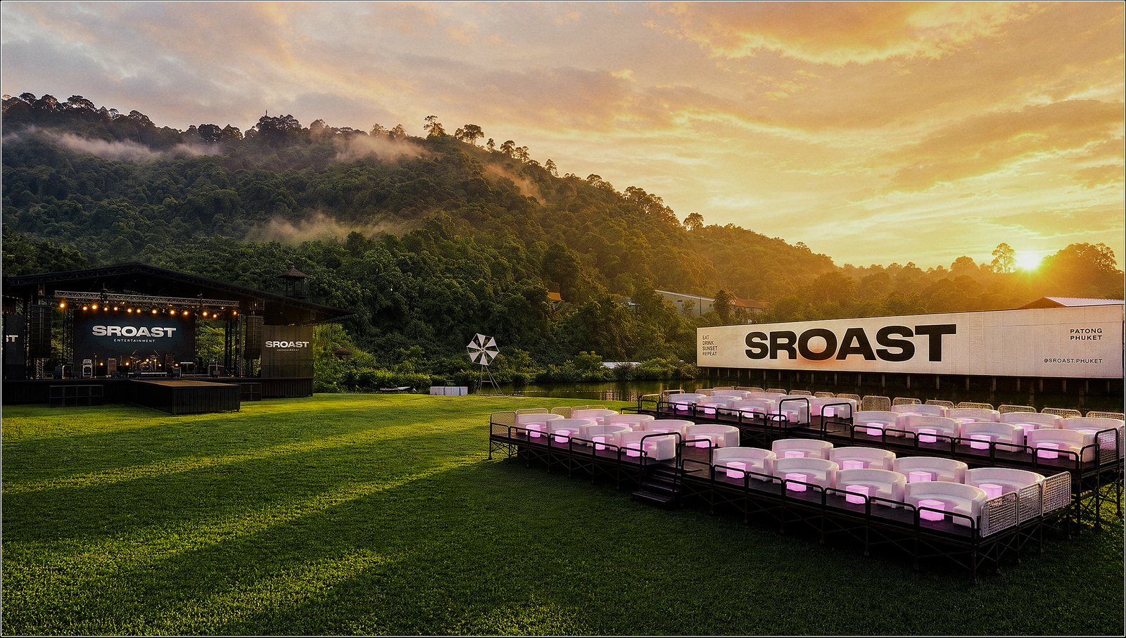 The venue at sunset — lawn, stage, windmill and the SROAST billboard across the lake.